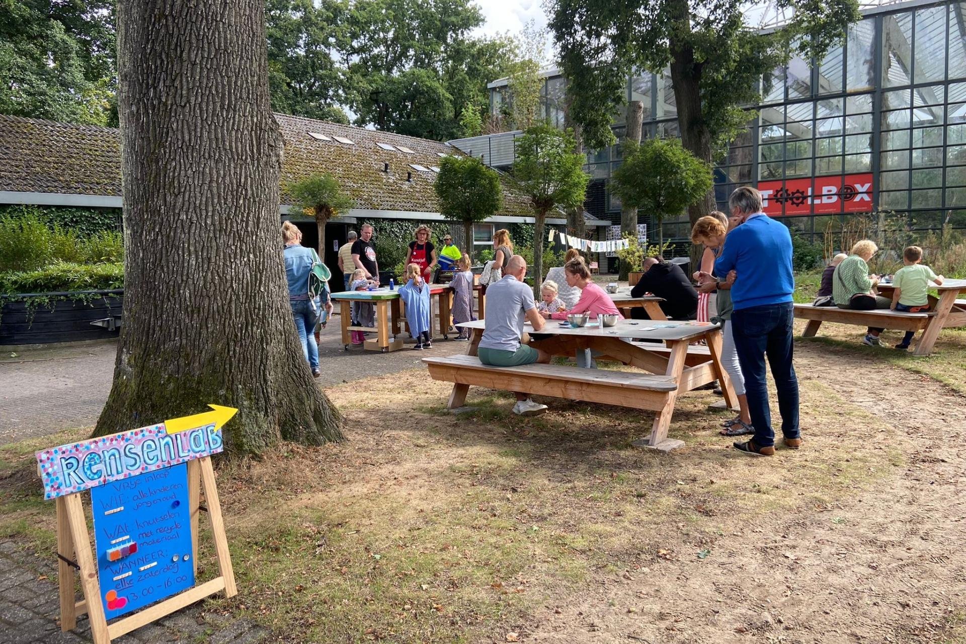 Kinderen en volwassenen aan picknicktafels aan het werk met papier en drukinkt.