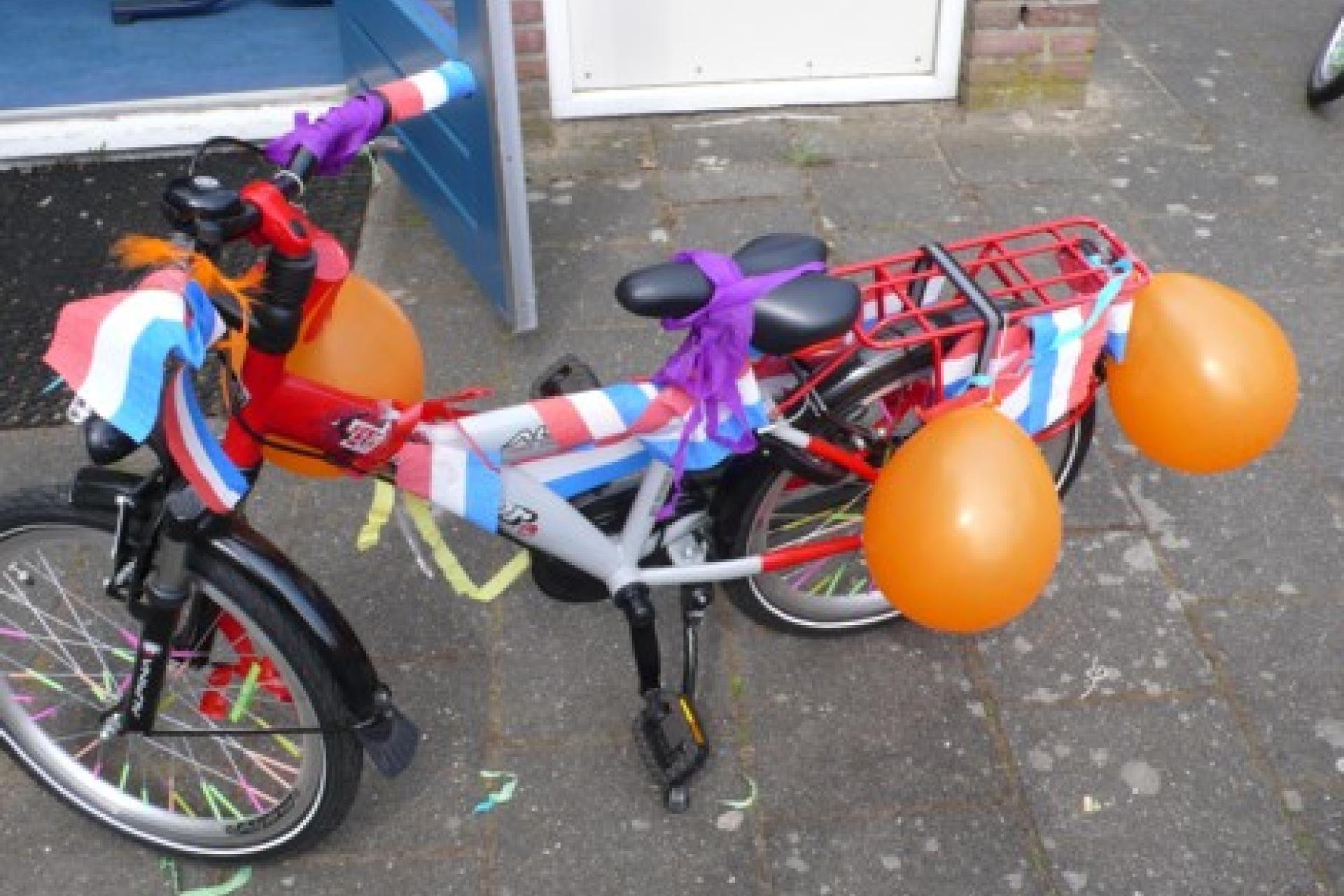 Een versierde fiets met rood-wit-blauwe slingers en oranje ballonnen